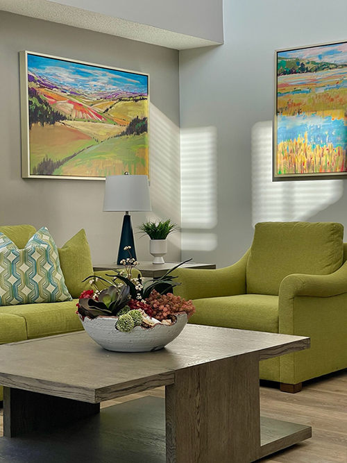 Image featuring the new community space with green chairs and vibrant landscape paintings.
